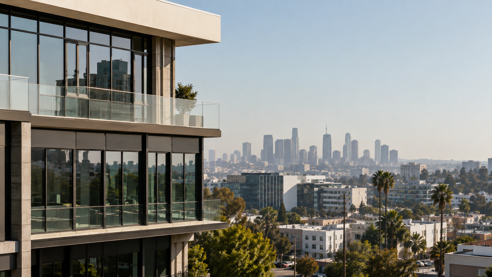 Glass-and-concrete commercial building in the foreground with the Los Angeles skyline beyond.