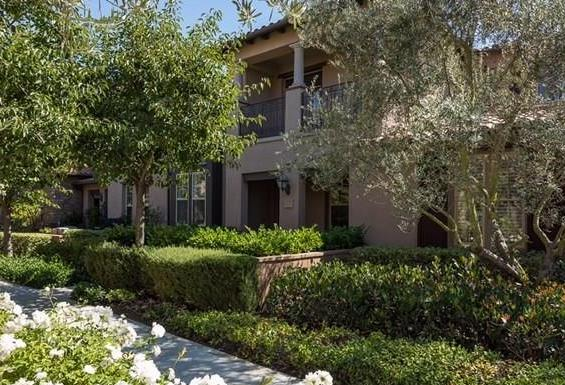 The funded Newport Coast residence: an attached Mediterranean-style home behind mature olive trees and hedges.